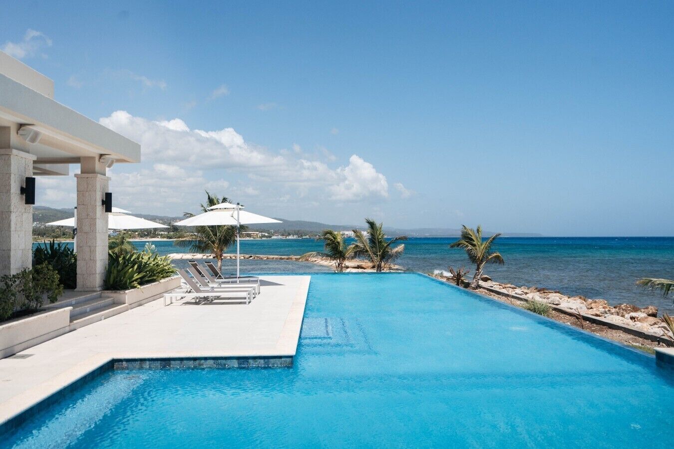 Piscina con vista al mar, sillas de descanso y sombrillas.