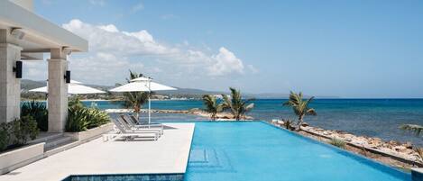 Piscina con vista al mar, sillas de descanso y sombrillas.