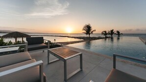 Un espace aménagé au bord de la piscine, avec des chaises longues et une vue sur le coucher de soleil sur l’océan.