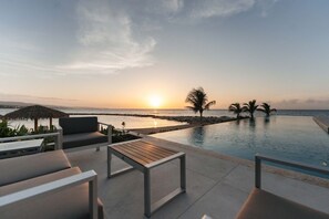 A poolside area with lounge chairs and a view of the sunset over the ocean. - Ocean View | 5BR Staffed Resort Villa by Bocobay (St. Ann’s Bay)