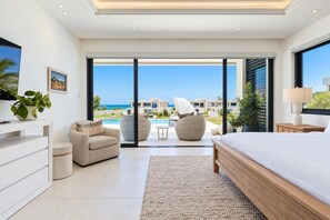 A modern bedroom with a large bed, a sofa, and a view of a pool and buildings. - Oceanview 5BR Pool Villa | Private Chef, Butler | Villa LayLow by Bocobay (St. Ann’s Bay)