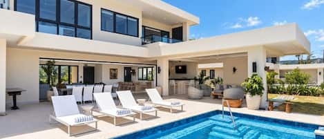 Un bâtiment moderne à deux étages doté d’une piscine, d’un espace extérieur aménagé et d’un bar.