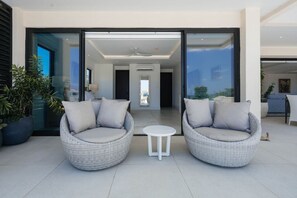 A modern outdoor seating area with wicker chairs and a small table, connected to a building with glass doors. - Ocean View | 5BR Staffed Resort Villa by Bocobay (St. Ann’s Bay)