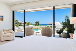 A bedroom with a large bed, two wicker chairs, a small table, and a view of a pool and ocean. - Oceanview 5BR Pool Villa | Private Chef, Butler | Villa LayLow by Bocobay (St. Ann’s Bay)