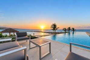 A poolside area with a sunset view, lounge chairs, and a thatched umbrella. - Ocean View | 5BR Staffed Resort Villa by Bocobay (St. Ann’s Bay)