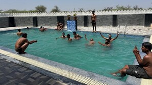 En swimmingpool med mennesker i og omkring den, en flisebeklædt væg og en klar himmel.