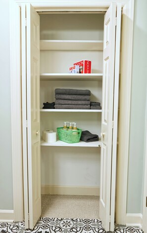 Ein begehbarer Kleiderschrank mit Regalen, auf denen gefaltete Handtücher liegen, einem Tablett mit Pflegeprodukten und einer Schachtel Pflaster.
