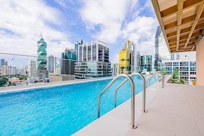 Ein Pool auf dem Dach mit Blick auf einen Stadt-Horizont, inklusive moderner Gebäude und einem markanten Turm.