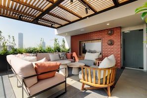 Um terraço no telhado com área de estar moderna ao ar livre, uma janela grande e vista para a cidade.