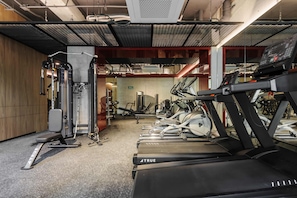 Uma academia com esteiras, aparelhos de musculação e um banco.