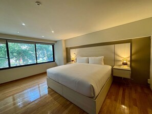 Ein modernes Schlafzimmer mit einem großen Bett, Nachttischlampen und Blick auf Bäume durch ein Fenster.