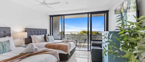 A modern hotel room with a large bed, a ceiling fan, a balcony with a view, and a TV mounted on the wall.
