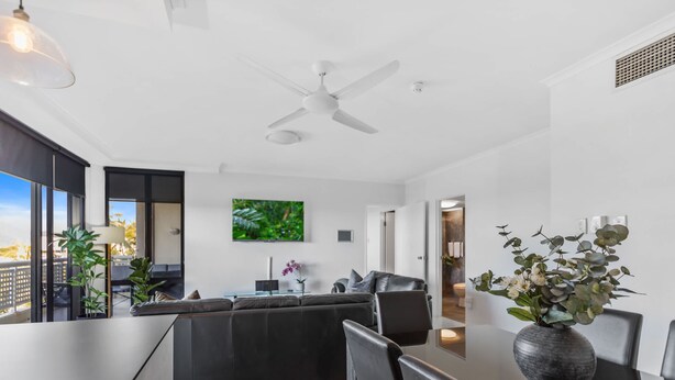 Uma sala de estar moderna com sofá, área de jantar com cadeiras, ventilador de teto e uma janela grande.