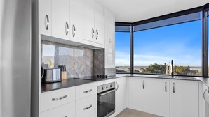 Uma cozinha moderna com armários brancos, forno embutido e uma janela grande com vista para o exterior.