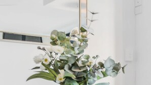 Um interior moderno com uma mesa de vidro, um vaso escuro com flores e um espelho na parede.