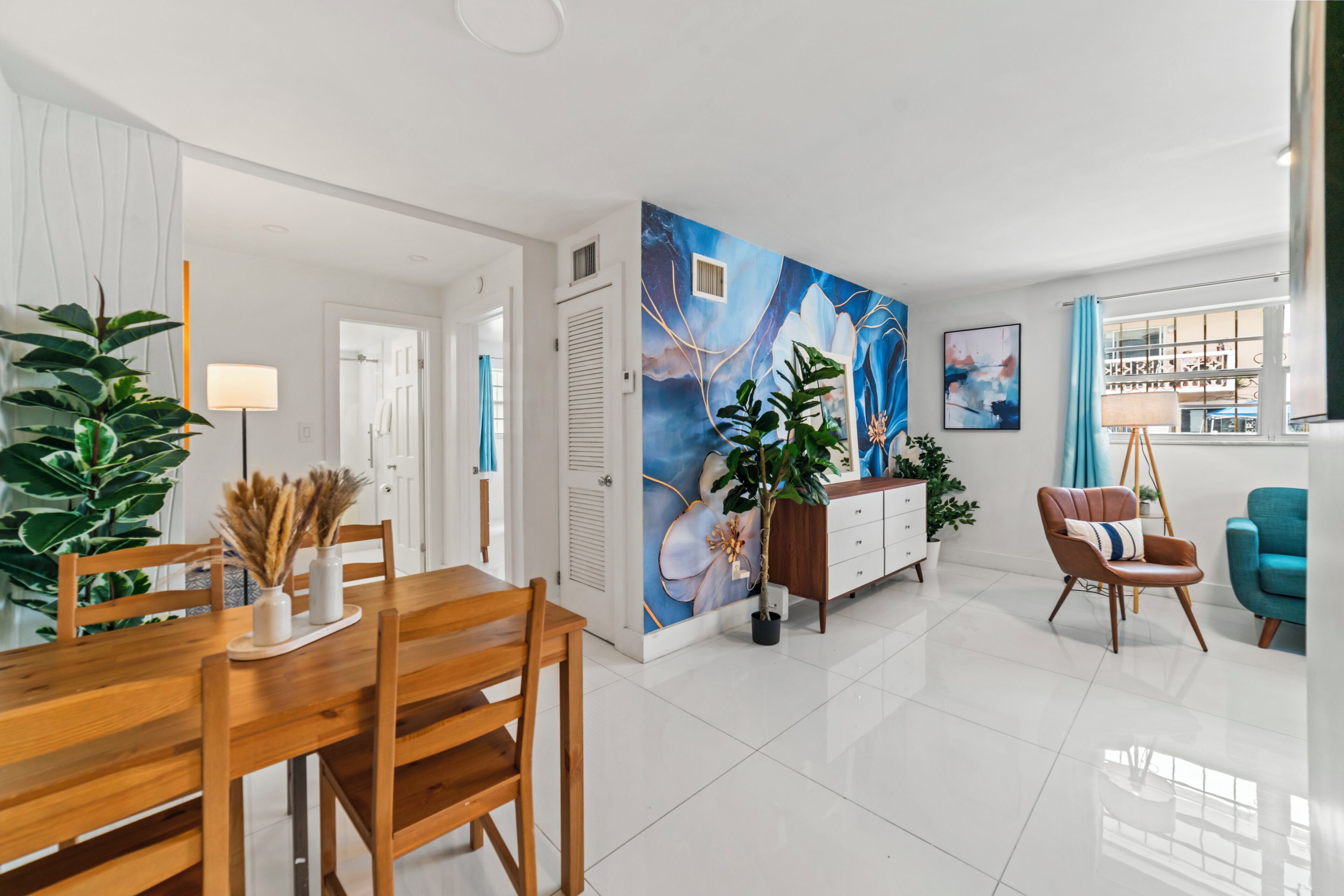 A modern living room with a dining area, featuring a large abstract mural, a wooden dining table, and a blue armchair.