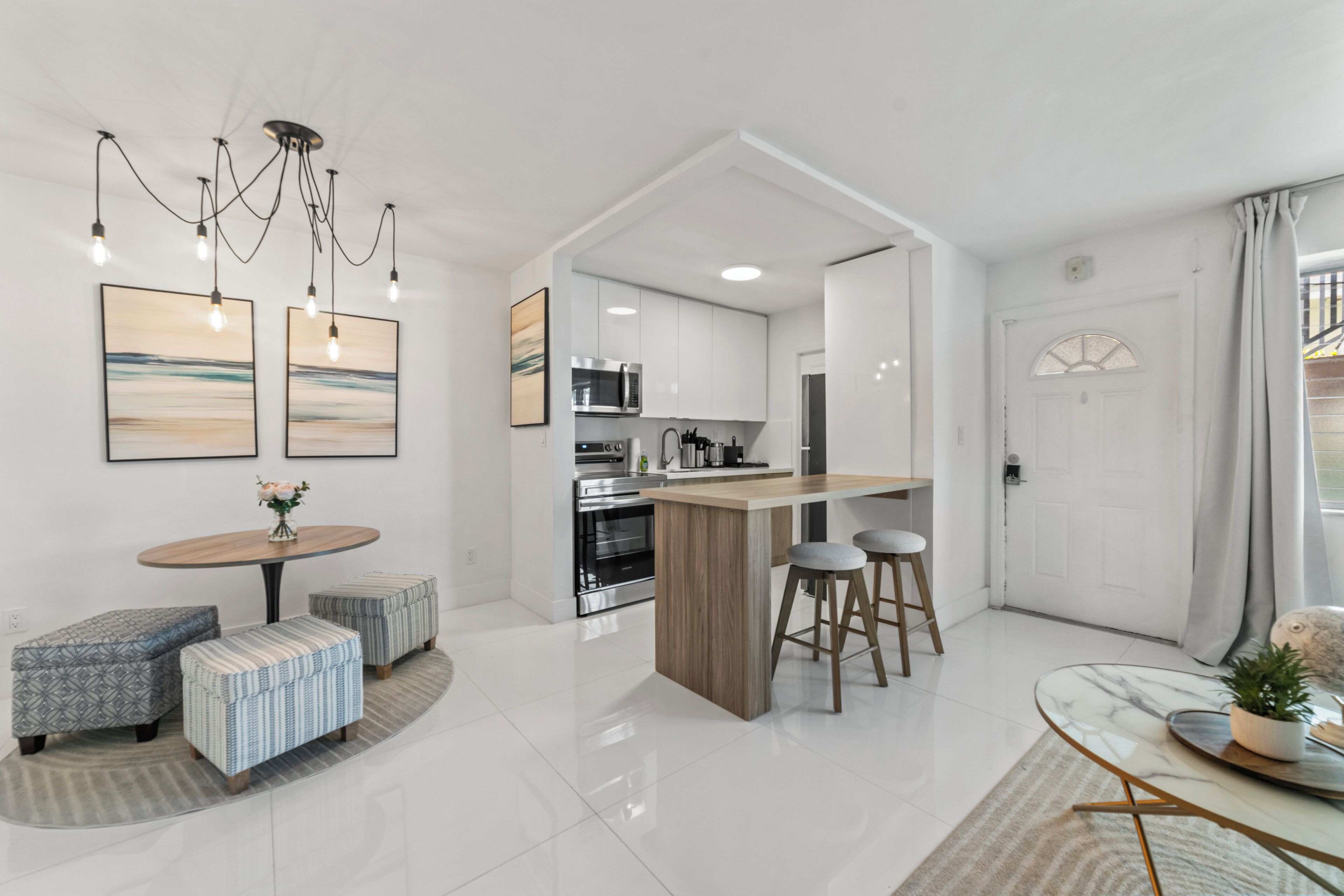 Uma cozinha moderna com eletrodomésticos de aço inoxidável, uma ilha de madeira com banquetas e uma área de jantar com mesa redonda e pufes.
