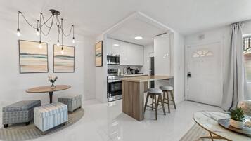 Uma cozinha moderna com eletrodomésticos de aço inoxidável, uma ilha de madeira com banquetas e uma área de jantar com mesa redonda e pufes.