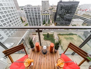 A balcony with a wooden table, two chairs, potted plants, and a city view. - Warsaw Home With City Views (Warsaw)