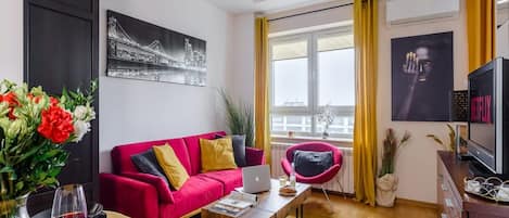 Una sala de estar moderna con un sofá rojo, una mesita de centro, una computadora portátil y un televisor.