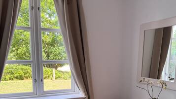 Ein Zimmer mit Fenster, Stuhl, Kommode und Spiegel.