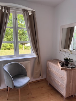 A room with a window, a chair, a dresser, and a mirror.