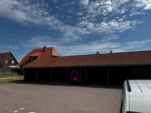 Edifici amb teulada vermella, zona de pàrquing coberta i un vehicle vermell aparcat a dins.