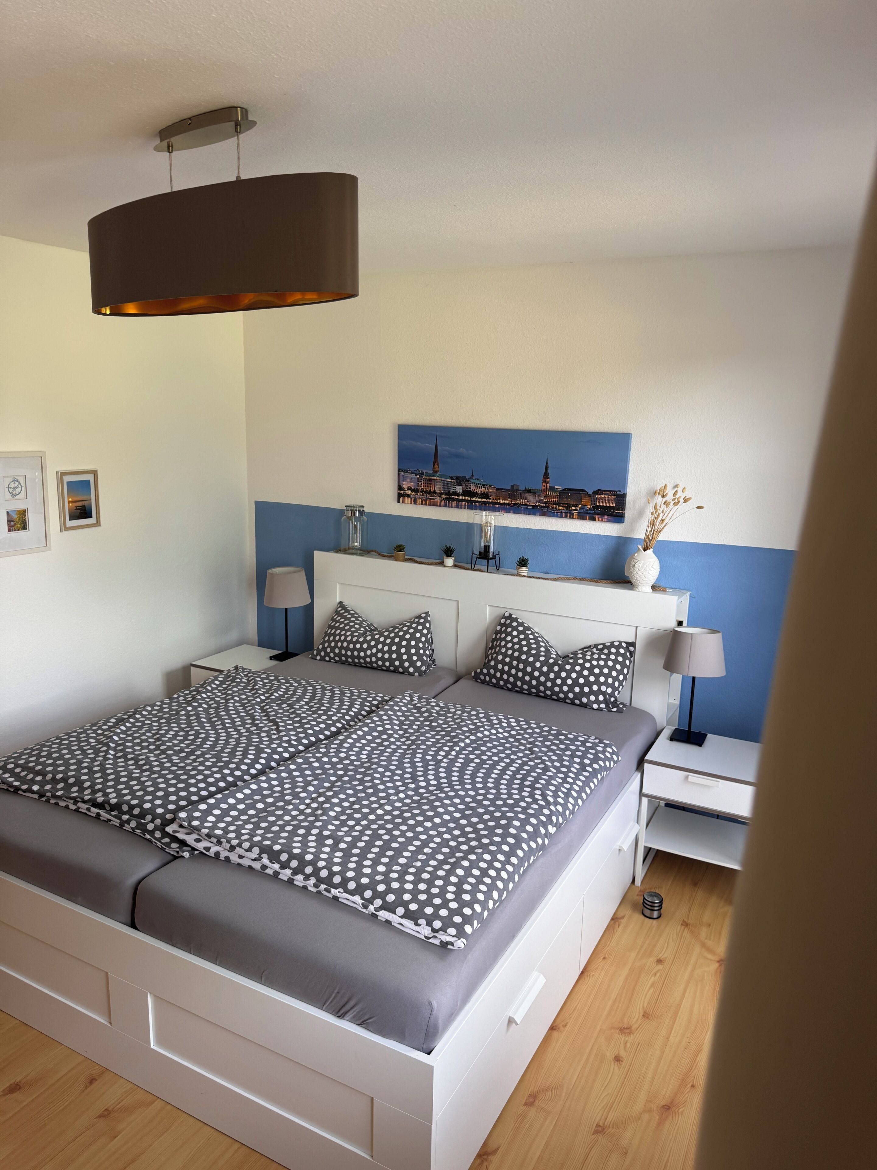 Ein Schlafzimmer mit einem Bett, Nachttischen, einer Lampe, einem Stadtbild und einer Deckenleuchte.
