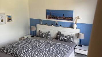 Une chambre à coucher avec un lit, des tables de chevet, une lampe, un tableau représentant un paysage urbain et un luminaire au plafond.