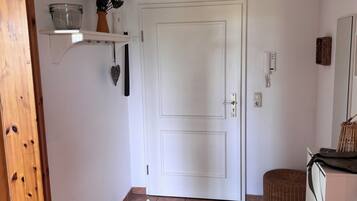Ein Zimmer mit einer weißen Tür, einem Regal mit einer Schüssel und einer Pflanze, einem Korbstuhl und einem weißen Gerät.