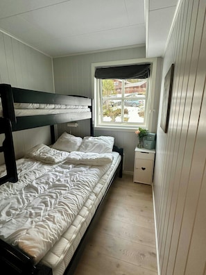 Ein Schlafraum mit Etagenbett, Fenster, Nachttisch und Pflanze.