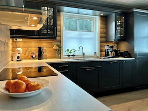 A modern kitchen with dark cabinetry, a large window, and a bowl of oranges on the counter. - Bright apartment in Kvasshaugen holiday park (Trøndelag)