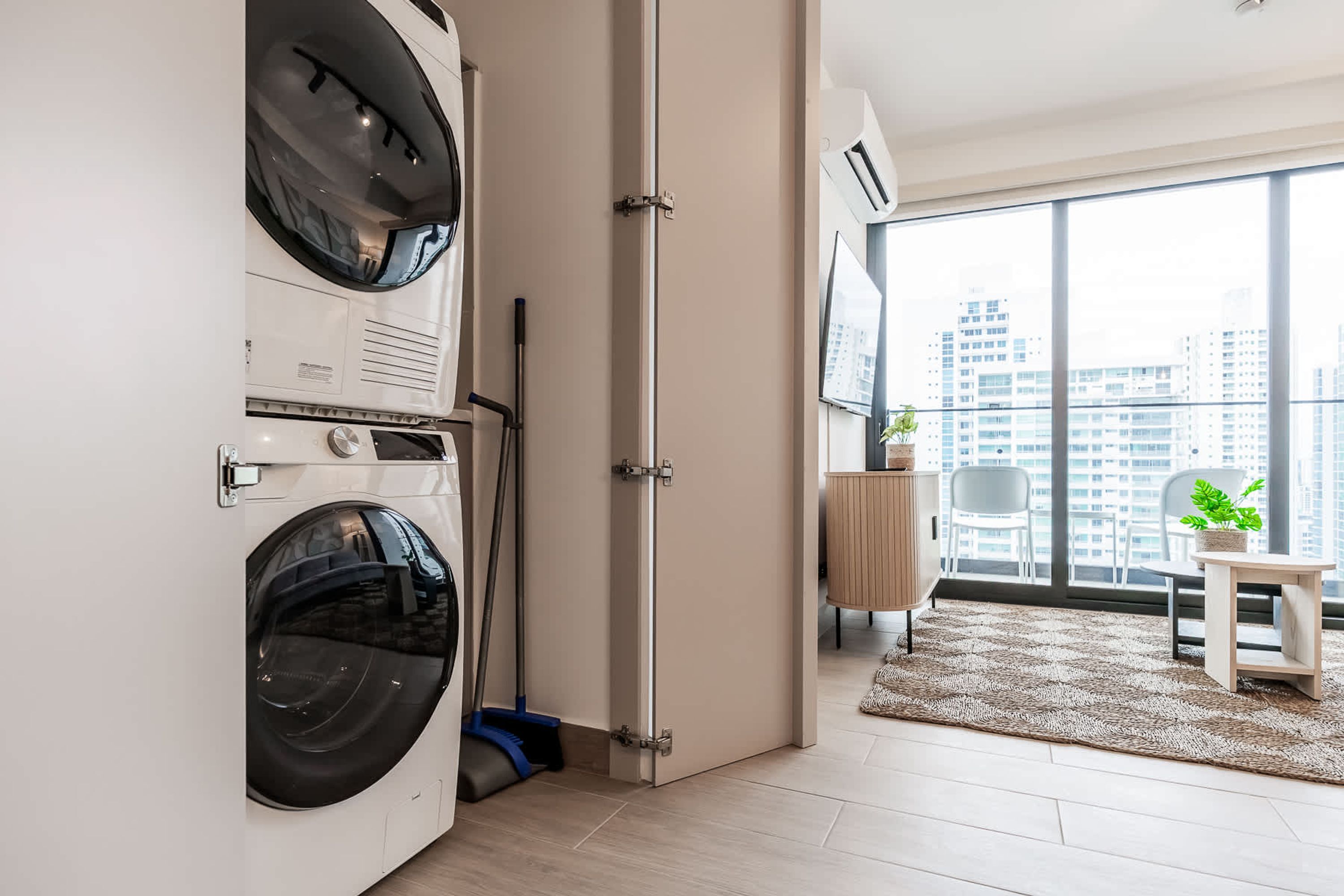 Un apartamento moderno con lavadero, un ventanal amplio con vistas a la ciudad y una pequeña zona de estar con una planta.