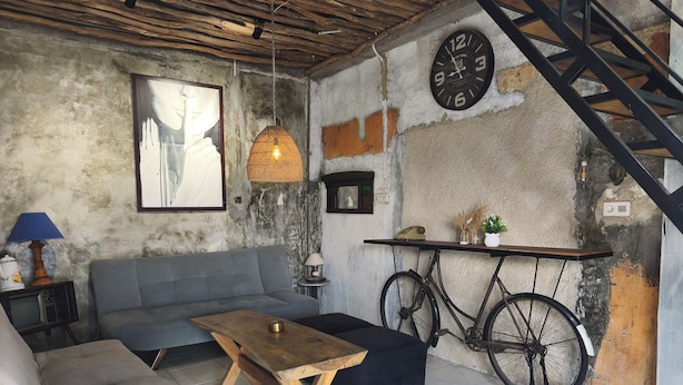 A rustic interior with a sofa, coffee table, bicycle, and a clock on the wall.