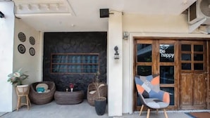 A building entrance with a stone wall, a wooden door with a 'Be happy' sign, and outdoor seating.