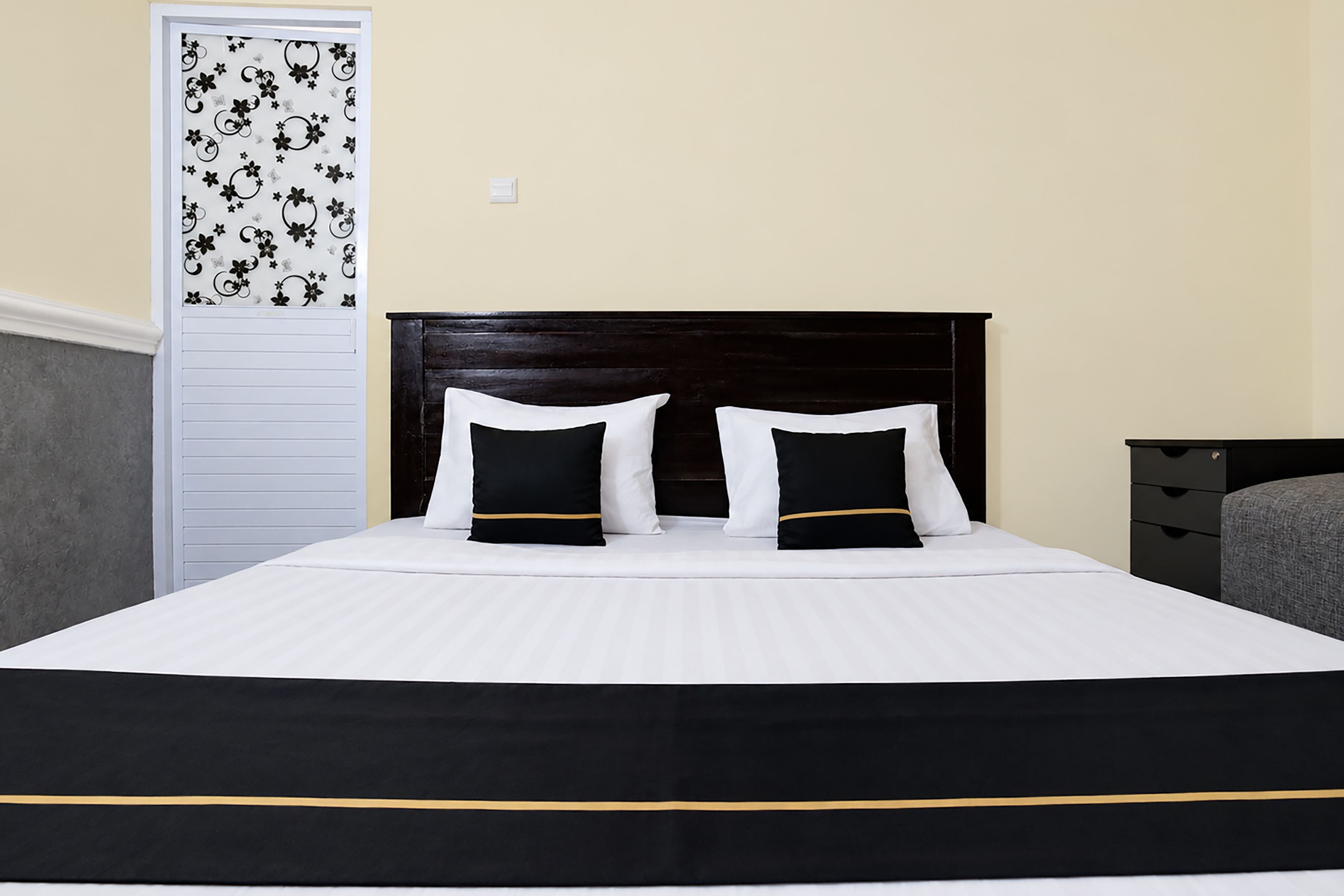 A bed with a black and white bedspread, two black pillows with gold trim, and a dark wooden headboard.