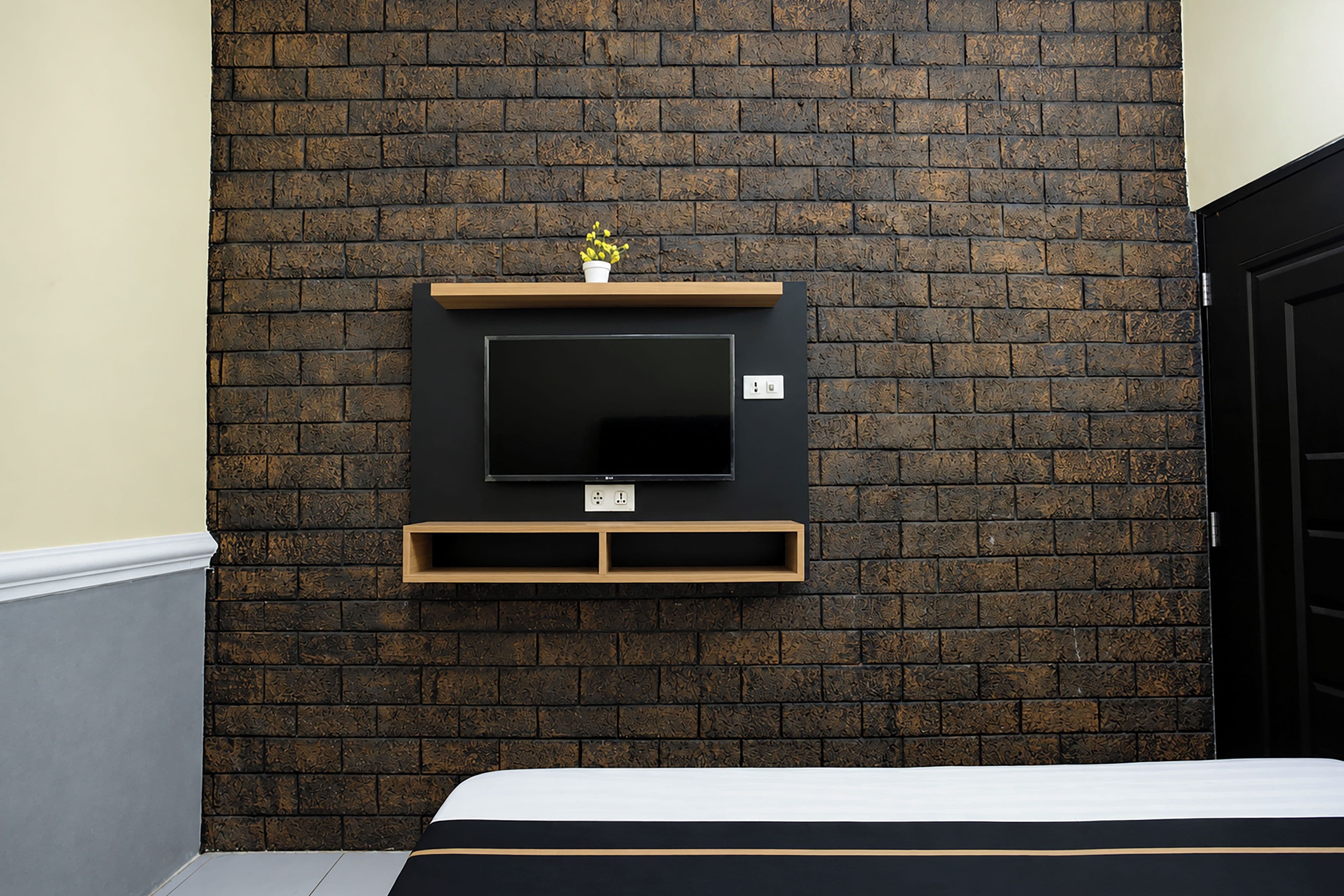 Quarto com parede de tijolos, televisão montada e cama com colchão branco.