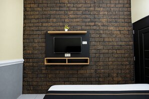A room with a brick wall, a mounted TV, and a bed with a white mattress.