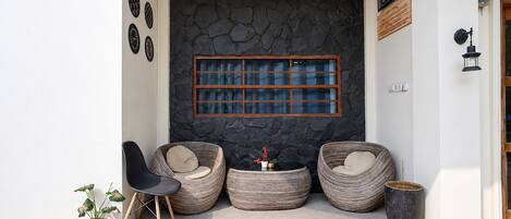 A modern outdoor seating area with three wicker chairs, a small table, and a potted plant.