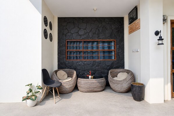 A modern outdoor seating area with three wicker chairs, a small table, and a potted plant.
