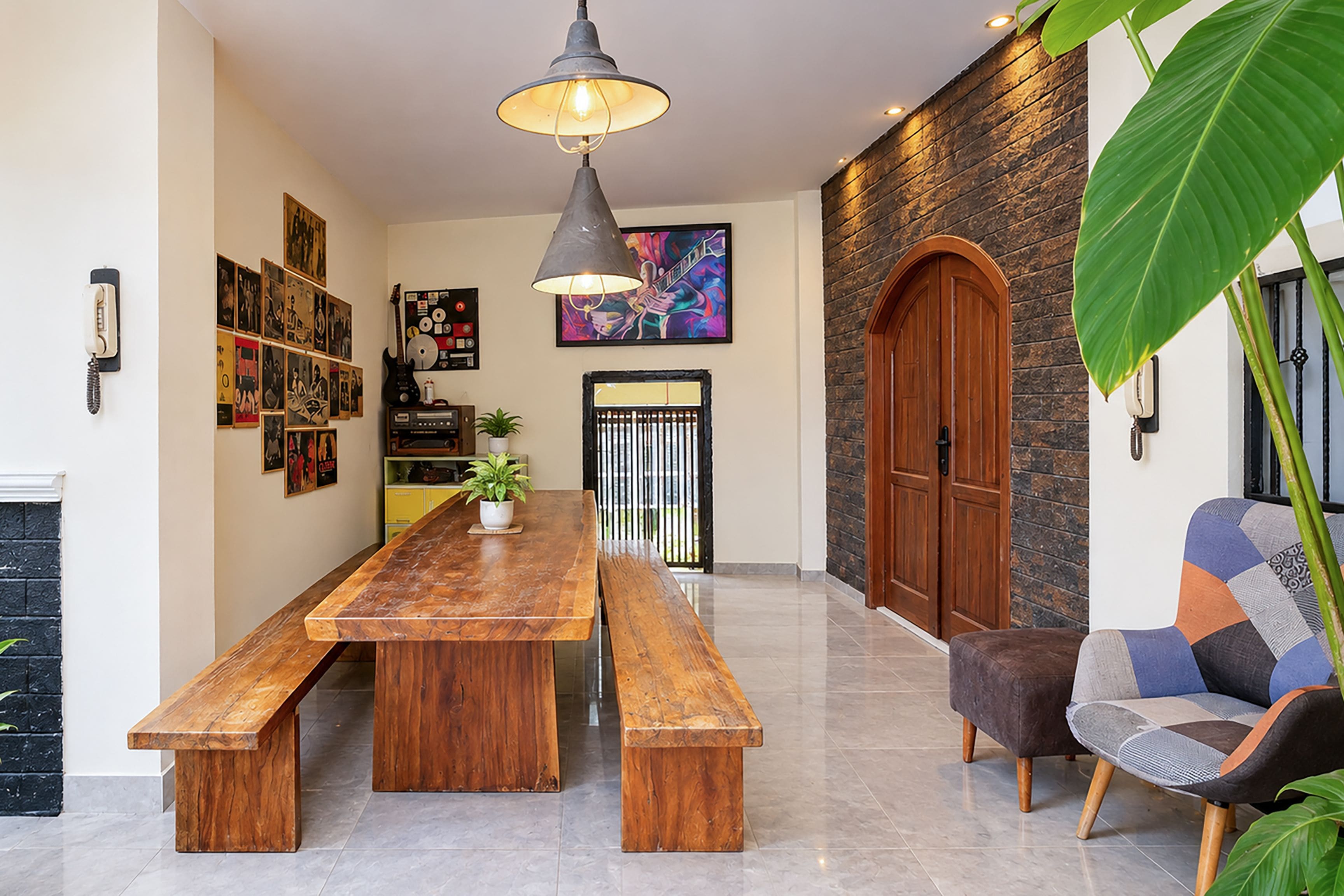Una habitación amplia con una larga mesa de madera para comer, un banco, una silla moderna, una lámpara colgante y una planta grande.