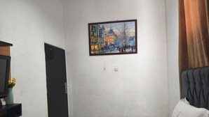 A hotel room with a bed, a painting on the wall, a door, and a curtain.