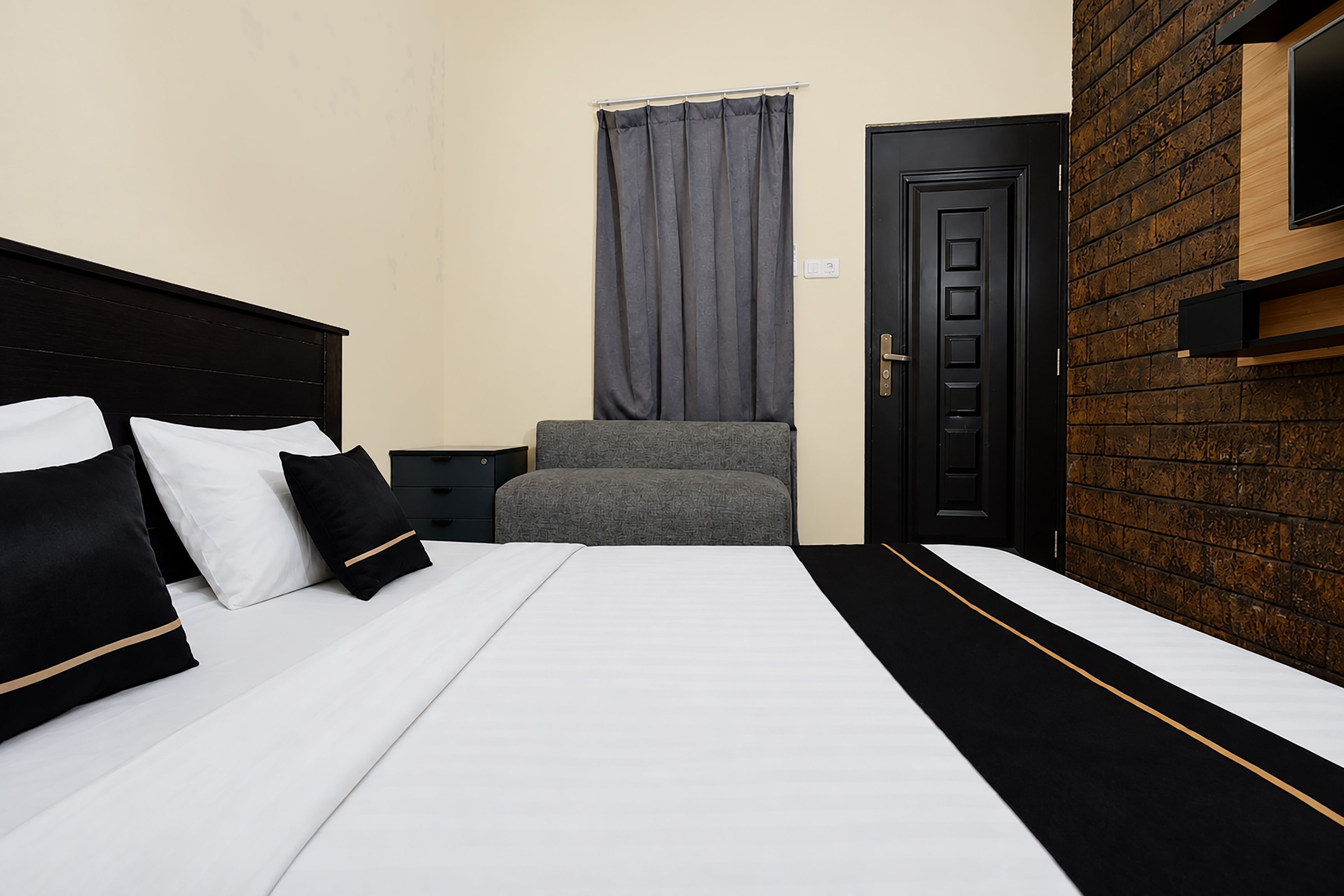Habitación de hotel con una cama, una silla, una puerta y un televisor montado en la pared.