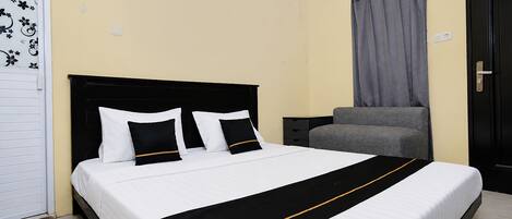 Una habitación de hotel con una cama, una mesita de noche, un sofá gris y una puerta negra.