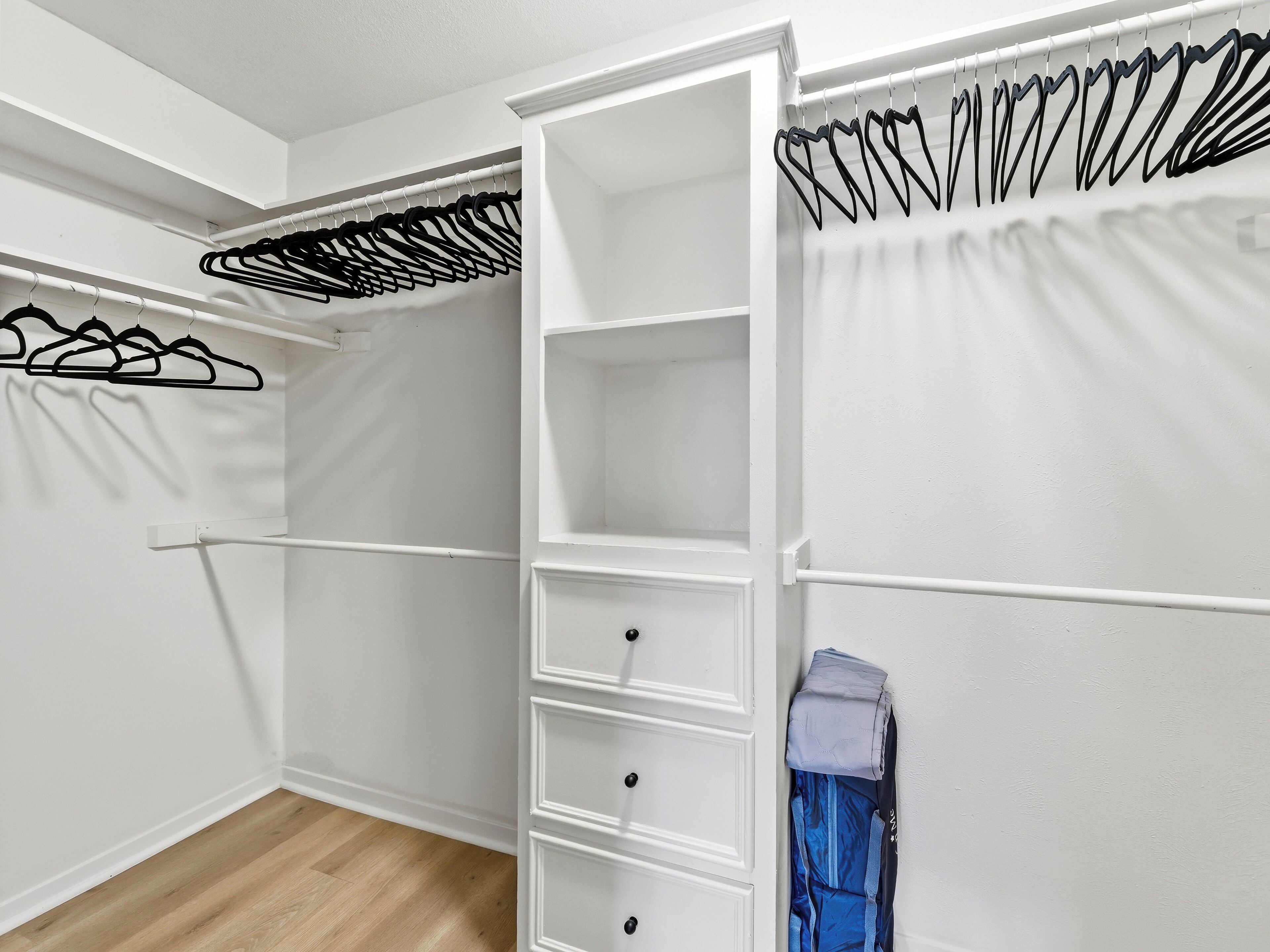 Ein begehbarer Kleiderschrank mit weißen Regalen, einer Kleiderstange und einem gefalteten Kleidungsstück auf der rechten Seite.