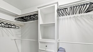 Ein begehbarer Kleiderschrank mit weißen Regalen, einer Kleiderstange und einem gefalteten Kleidungsstück auf der rechten Seite.