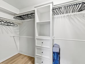 Ein begehbarer Kleiderschrank mit weißen Regalen, einer Kleiderstange und einem gefalteten Kleidungsstück auf der rechten Seite.