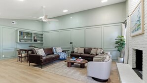 Ein Wohnzimmer mit Kamin, Deckenventilator, Essbereich mit Tisch und Stühlen sowie Bücherregal.