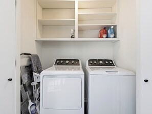 Ein Waschraum mit zwei Waschmaschinen, einem Trockner und einem oberhalb angebrachten Hängeschrank für Reinigungsmittel.