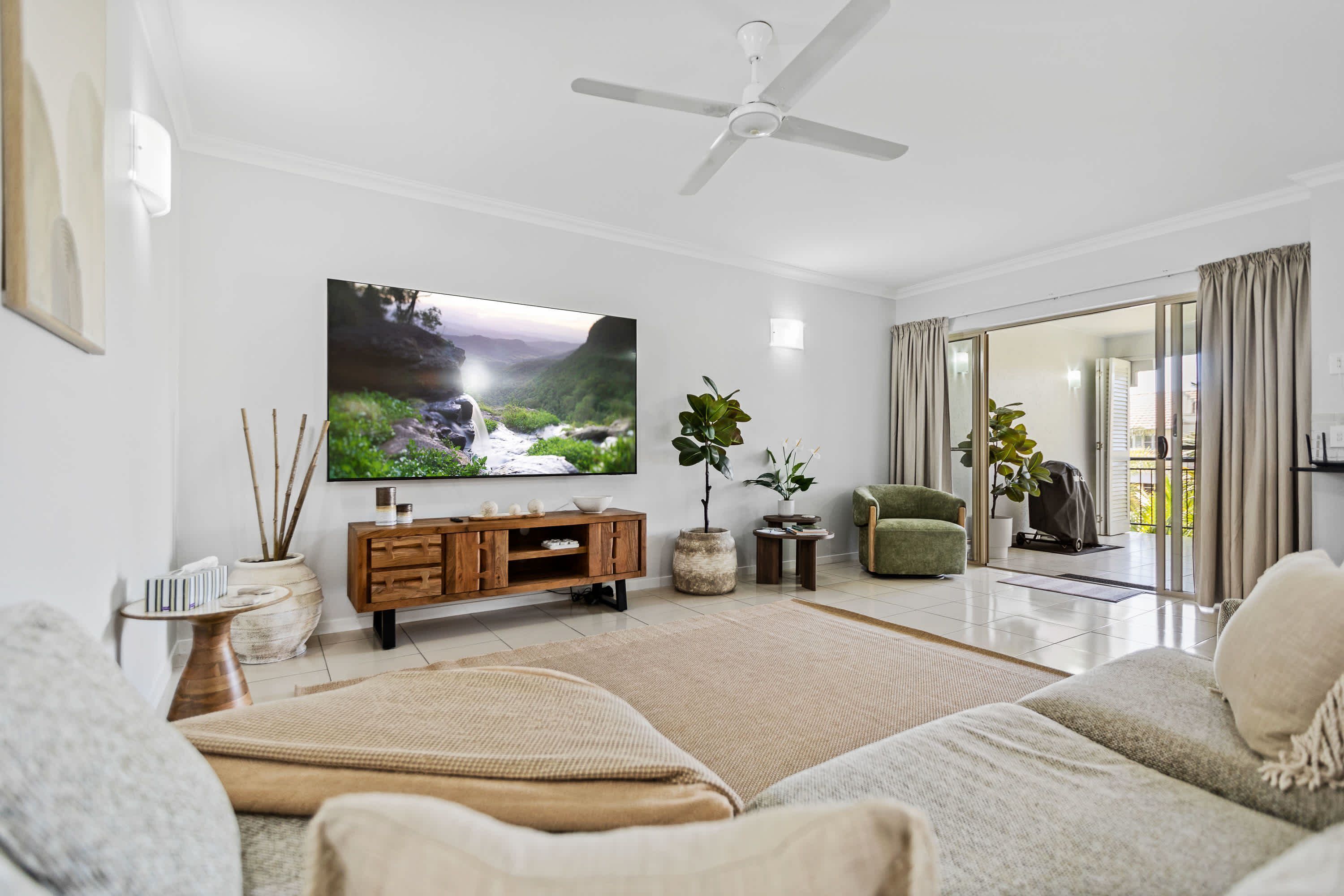 A modern living room with a flat-screen TV, a ceiling fan, a green armchair, and a sliding glass door leading to an outdoor area.